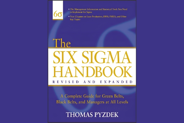 A professional reading the Six Sigma Handbook by Thomas Pyzdek, surrounded by charts and graphs